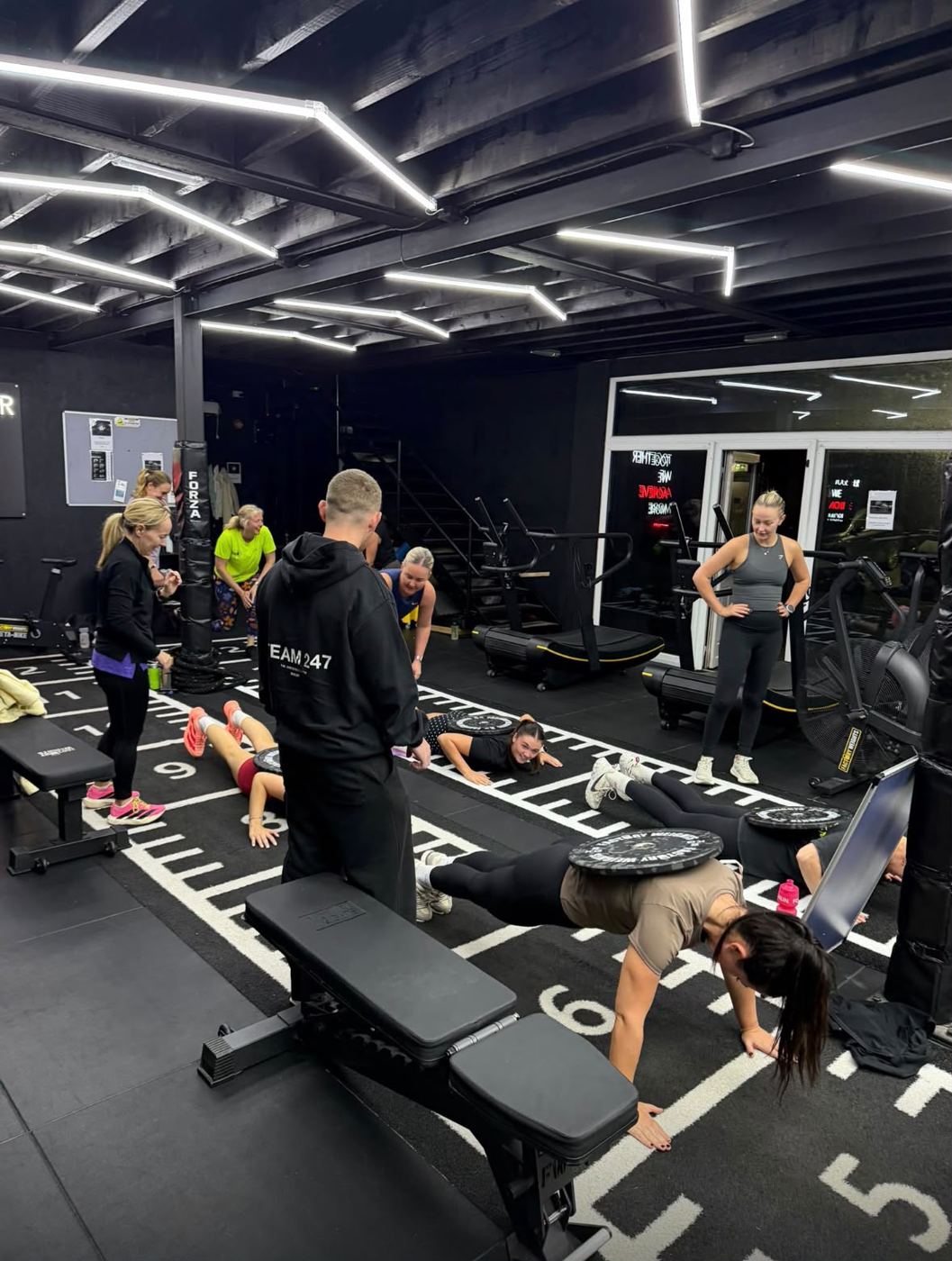 Ally coaching a Hyrox class through plate-loaded plank work at Achieve Studio